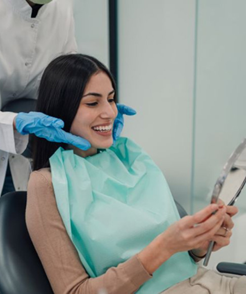 Happy cosmetic dentistry patient admiring her smile in mirror