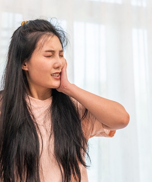 Woman in pink shirt rubbing jaw in pain