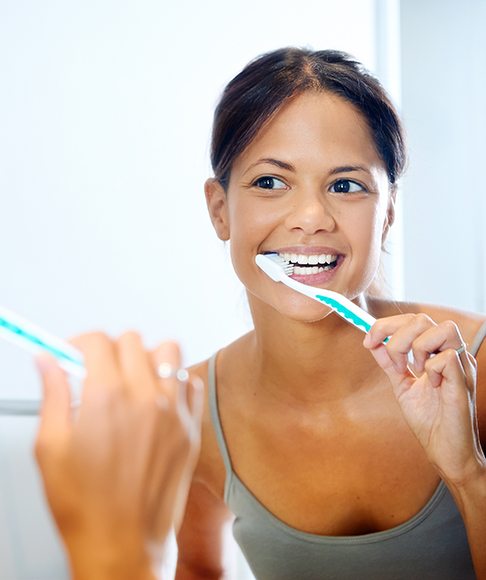 Woman in grey shirt brushing her teeth