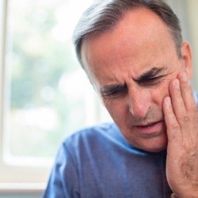 Man with lost dental crown holding cheek in pain