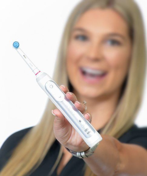 Dental team member holding up electric toothbrush that can help prevent dental emergencies