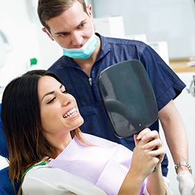 Dental patient holding mirror looking at her teeth