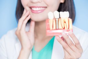 Dentist holding her face in the background and holding a model dental implant in the foreground